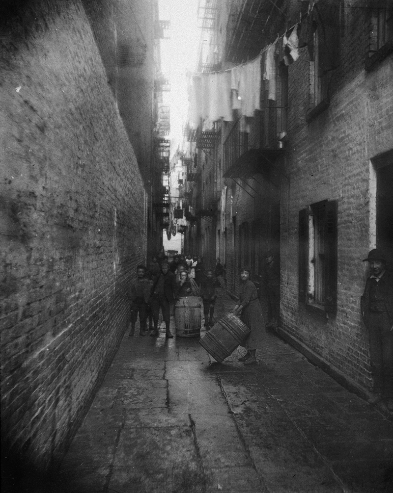 circa 1890:  Children play with barrels in an alley between tenement buildings in Gotham Court, 38 Cherry Street, New York City.  (Photo by Jacob A. Riis/Museum of the City of New York/Getty Images)