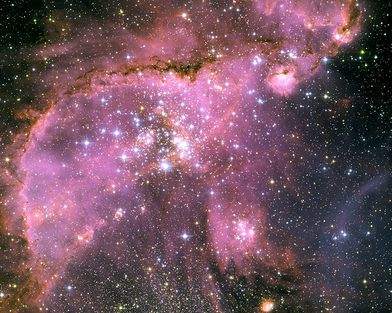 This Hubble Space Telescope view shows one of the most dynamic and intricately detailed star-forming regions in space, located 210,000 light-years away in the Small Magellanic Cloud (SMC), a satellite galaxy of our Milky Way. At the centre of the region is a brilliant star cluster called NGC 346. A dramatic structure of arched, ragged filaments with a distinct ridge surrounds the cluster.   A torrent of radiation from the hot stars in the cluster NGC 346, at the centre of this Hubble image, eats into denser areas around it, creating a fantasy sculpture of dust and gas. The dark, intricately beaded edge of the ridge, seen in silhouette, is particularly dramatic. It contains several small dust globules that point back towards the central cluster, like windsocks caught in a gale.